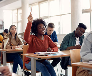 Image of young woman raising her hand in a classroom full of students.