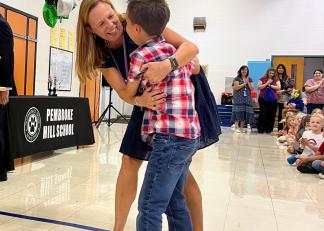 Liz Duclos hugs her son during a special ceremony Thursday recognizing her as New Hampshire's 2024 Teacher of the Year.